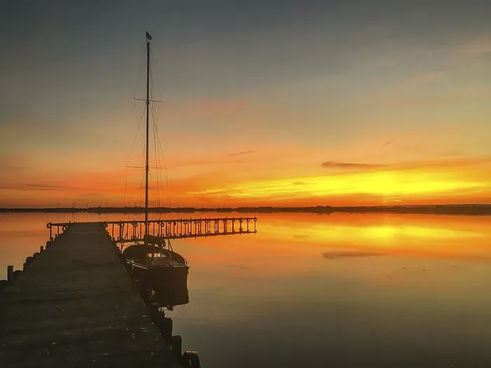 Stampa con cornice : Lago Dummer tranquillo con molo e barca a vela al tramonto. Stampa con cornice : Lago Dummer tranquillo con molo e barca a vela al tramonto.