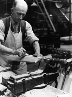 Stampe di Un fabbro di bastoni da cricket ad Accrington, Lancashire, Inghilterra che utilizza l'osso del fianco di un cervo per levigare il bastone. Anno: 1930 Renna Stampe: Fare bastoni di cricket
