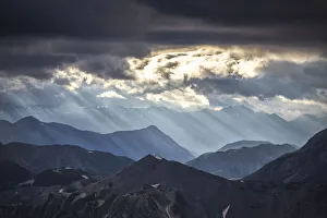 Europe Mountain Scenery Stampe: Sun rays filter between black clouds at sunset