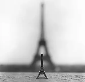 Stampe di Immagine a colori nero e bianco di una statuetta della Torre Eiffel si trova su un davanzale nel Trocadéro, con l'ombra della vera Torre Eiffel che sorge alle sue spalle Architettura Internazionale Stampe: Torre Eiffel, grande e piccola.