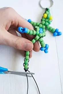 Creare anello da chiave con lucertola ricamata a perle, tagliando la cordicella in eccesso con le forbici.