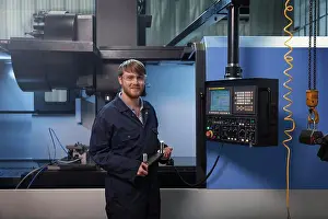 Stampe di L'apprendista tiene un cinturone a U davanti alla macchina CNC Novembre Stampe: L'apprendista tiene un cavo a U davanti alla macchina CNC.