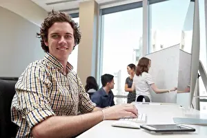 Office Communication Skills Stampe: Young man using computer in office looking towards camera