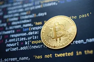 Cryptocurrency Symbol Stampe: Bitcoin coin placed on top of a black screen filled with colorful programming code