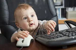 Young Boy At Desk Stampe: Boy, 10 months, using a computer mouse and keyboard