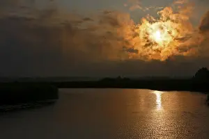 Dramatic Evening Sky Stampe: Dramatic sunset behind clouds over a quiet river with golden reflection
