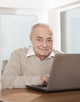 Man Smiling At Camera Stampe: Elderly man using a PC