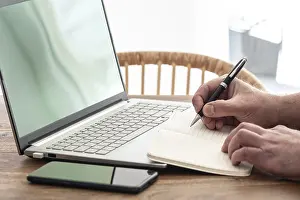 Man Working From Home Stampe: man taking notes on paper while using laptop computer