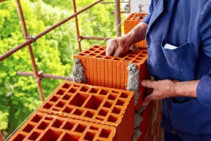 Construction Site Worker Stampe: Mason, bricklayer worker is using red blocks to mount a wall next the string line to be straight