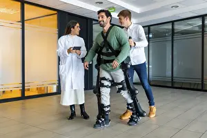 Young Adults With Disability Stampe: Mechanical exoskeleton, female doctor with device walking with disabled person with robotic skeleton in rehabilitation