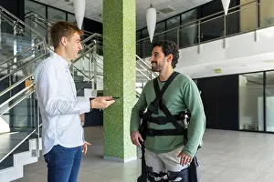 Mechanical Exoskeleton Stampe: Mechanical exoskeleton, physiotherapist looking at consultation with tablet with disabled person with robotic skeleton