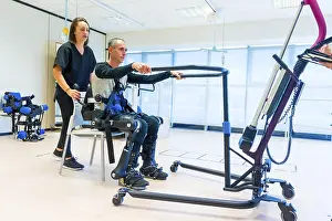 Mechanical Exoskeleton Stampe: Mechanical exoskeleton. Female physiotherapy doctor assistant lifting disabled person with robotic skeleton to get up
