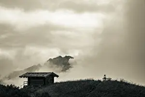 Female Hiker Stampe: Mountain hut with bench and climber and dramatic clouds in the background