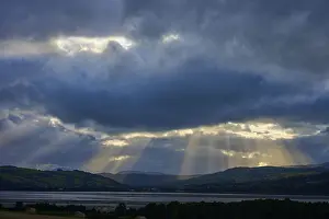 Light Breaking Through Clouds Stampe: Rays of light break through dramatic clouds over a lake and mountain landscape