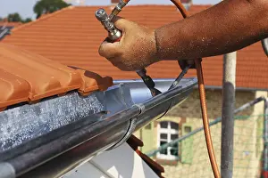 Residential Building Construction Site Stampe: Roofer doing tinsmith work on a gutter