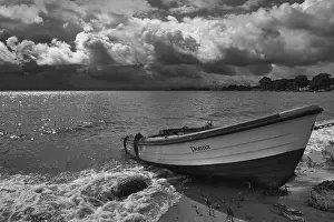 Deserted Sandy Beach Scene Stampe: Rowing boat on sandy beach in front of dramatic storm clouds