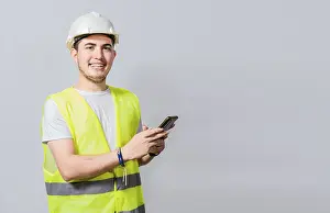 Construction Industry Professional Stampe: Smiling engineer using cell phone looking at camera