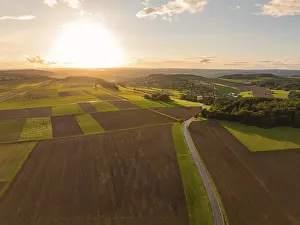 Dramatic Evening Sky Stampe: Sunset over sweeping fields with a winding road and dramatic sky