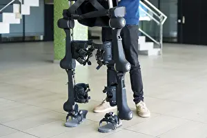 Exoskeleton Technology Stampe: Unrecognizable computer engineer in mechanical exoskeleton looking at the robot with a tablet