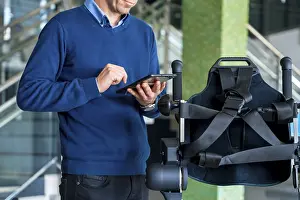Exoskeleton Technology Stampe: Unrecognizable computer engineer in mechanical exoskeleton looking at the robot with a tablet