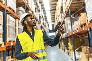 Supply Chain Management Stampe: Side view of an african worker scanning package with bar code reader in a distribution warehouse