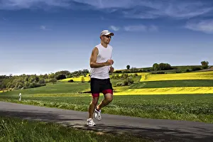 Fitness In Nature Stampe: A young man jogging through the fields